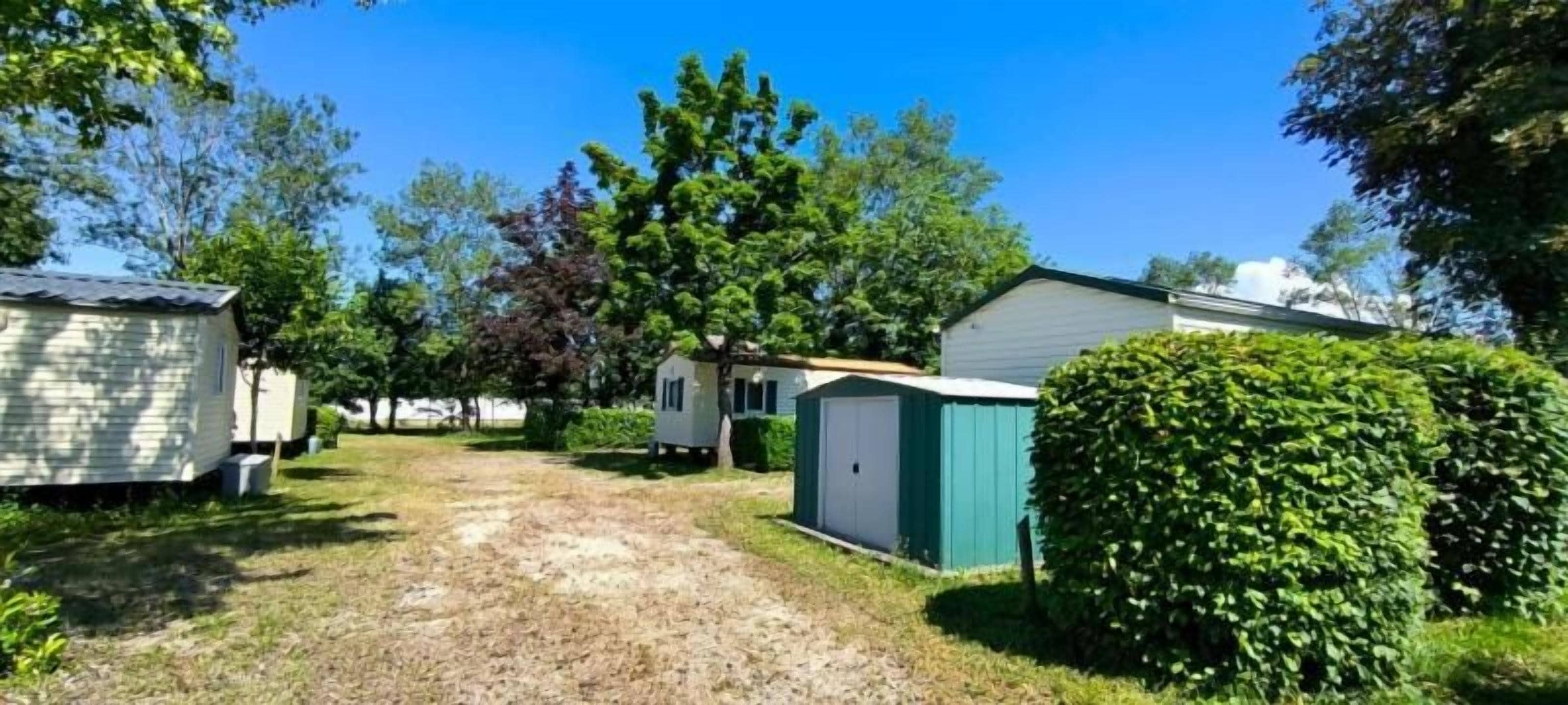 Un terrain de camping comprenant plusieurs mobil-homes, un chemin de gravier et des arbustes verdoyants.