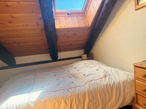 A bedroom with a sloped ceiling, a skylight, a bed with a floral bedspread, and a wooden dresser. - Apartment for 4 people near the slopes (La Salle-les-Alpes)