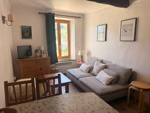 A cozy room with a sofa, a table, a TV, and a window with curtains. - Apartment for 4 people near the slopes (La Salle-les-Alpes)