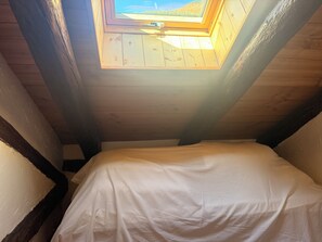 Ein Zimmer mit einem Oberlicht, Holzbalken und einem Bett mit weißer Bettdecke.