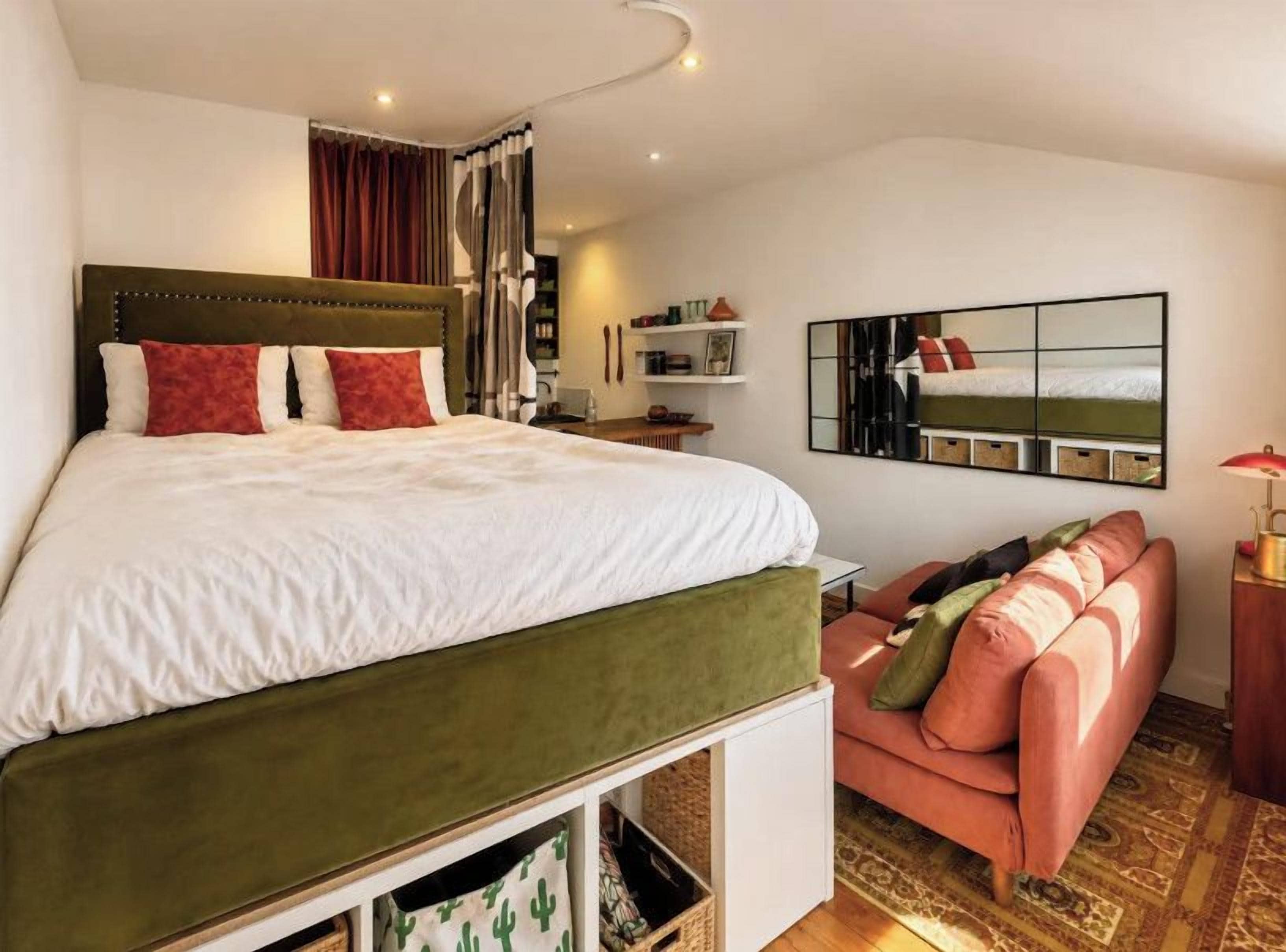 A bedroom with a bed, a sofa, a mirror, and a lamp.
