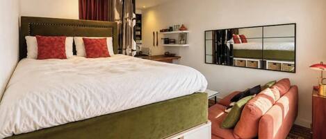 A bedroom with a bed, a sofa, a mirror, and a lamp.