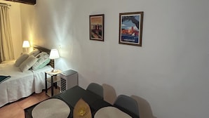 Habitación de hotel con cama, lámparas de noche, una mesa con sillas y dos cuadros en la pared.
