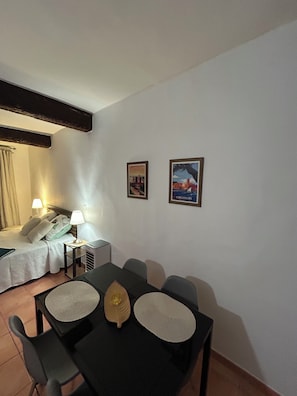 Habitación de hotel con cama, lámparas de noche, una mesa con sillas y dos cuadros en la pared.