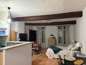 Un espacio habitable compacto con kitchenette, comedor, cama con un plaid verde y ventilador de techo.