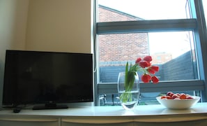 Ein Fernseher auf einem Schrank, eine Vase mit roten Tulpen und eine Obstschale auf einem Fensterbrett.