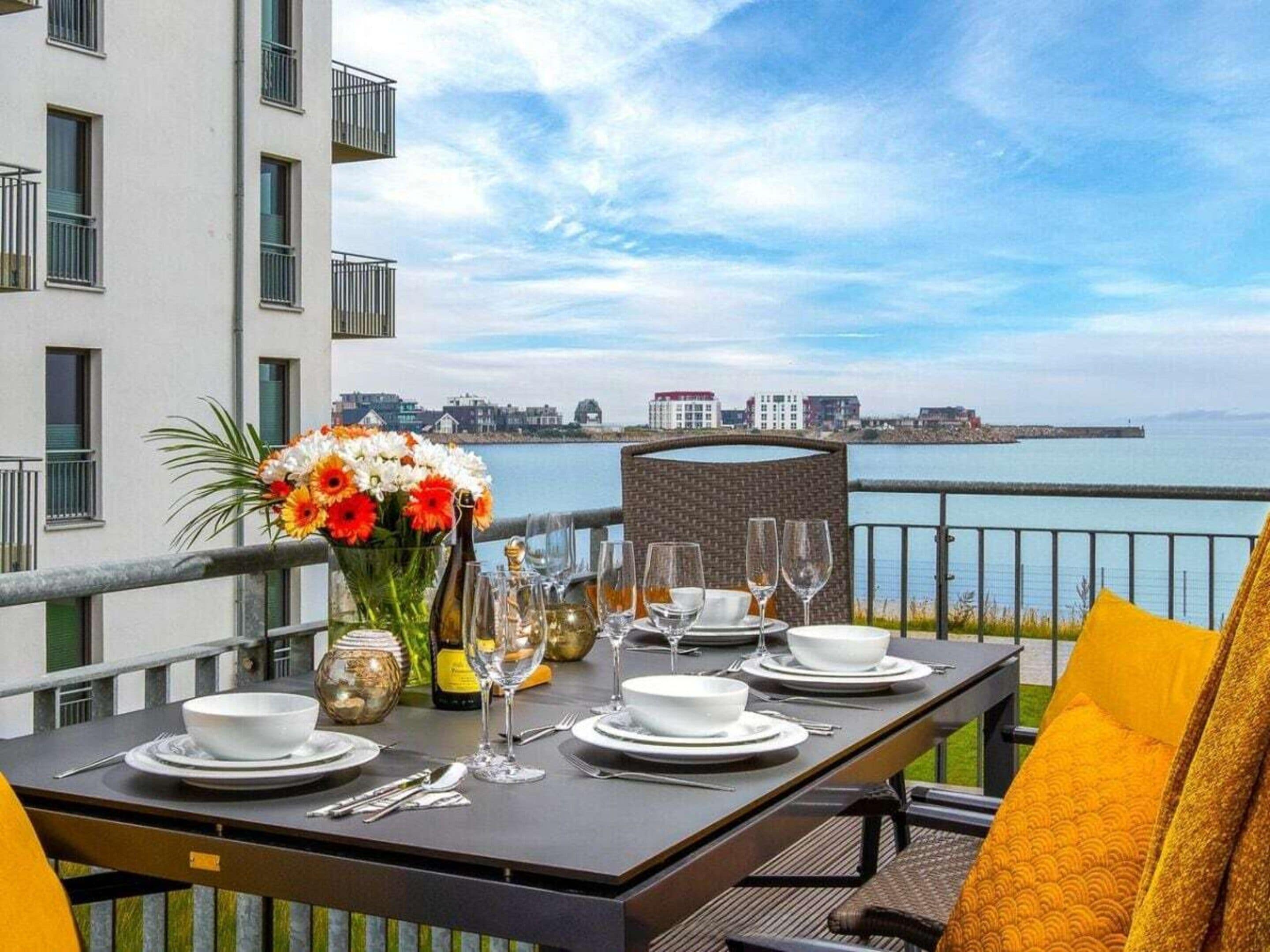 Une table dressée pour le dîner, avec vue sur la mer et des bâtiments en arrière-plan.