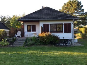 Ein einstöckiges Haus mit Ziegeldach, einer Veranda mit zwei Stühlen und einem Fahrrad davor.