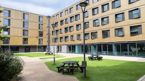 A multi-story building with a courtyard featuring picnic tables and a well-maintained lawn. - Student Only Palamon Court (Canterbury)