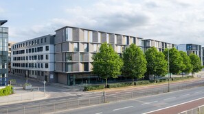 A modern multi-story building with a glass facade, surrounded by a road and a sidewalk. - Student Only Palamon Court (Canterbury)