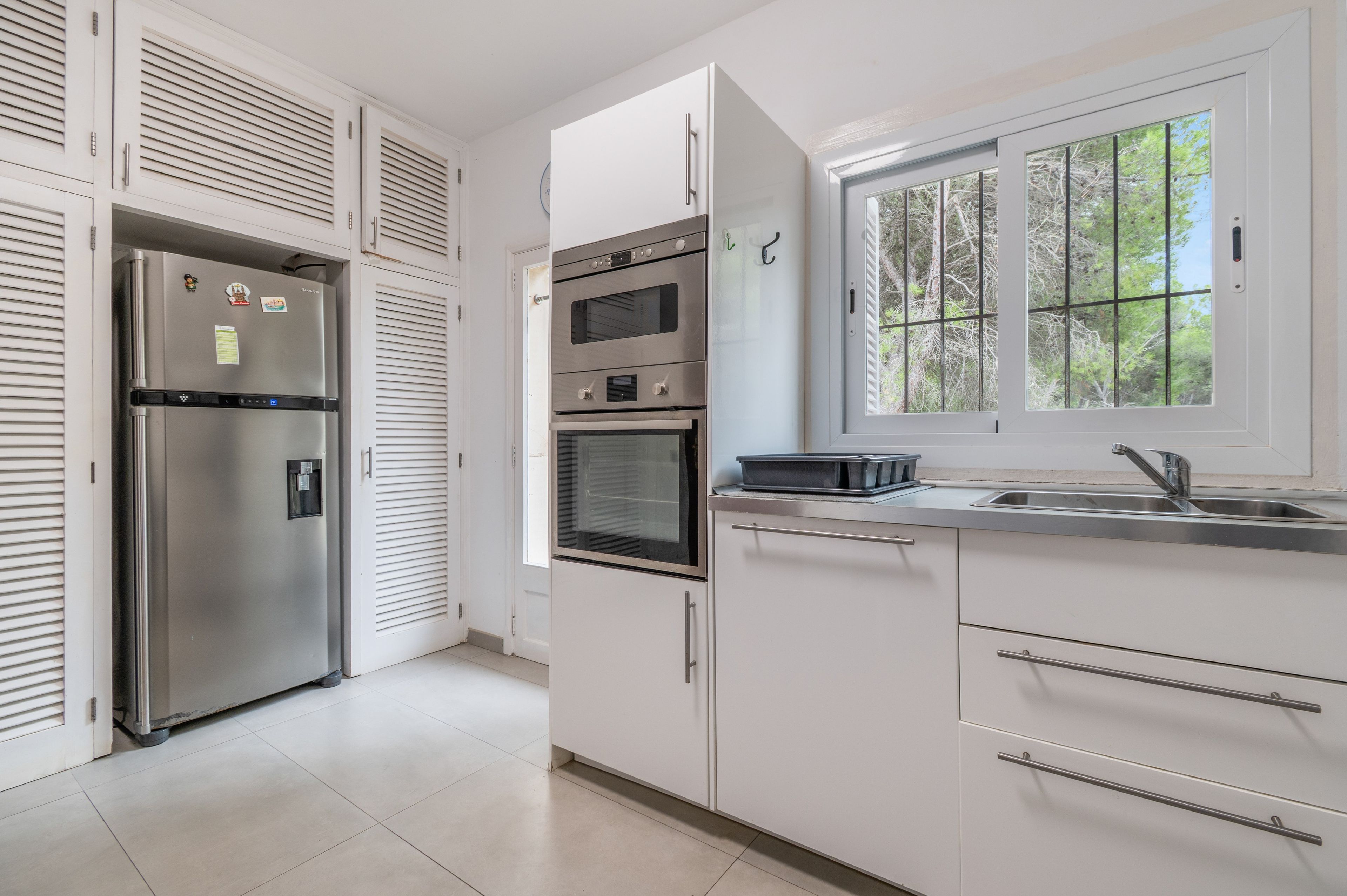 A modern kitchen with stainless steel appliances, a window with a view of trees, and white cabinetry.