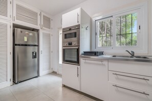 A modern kitchen with stainless steel appliances, a window with a view of trees, and white cabinetry.