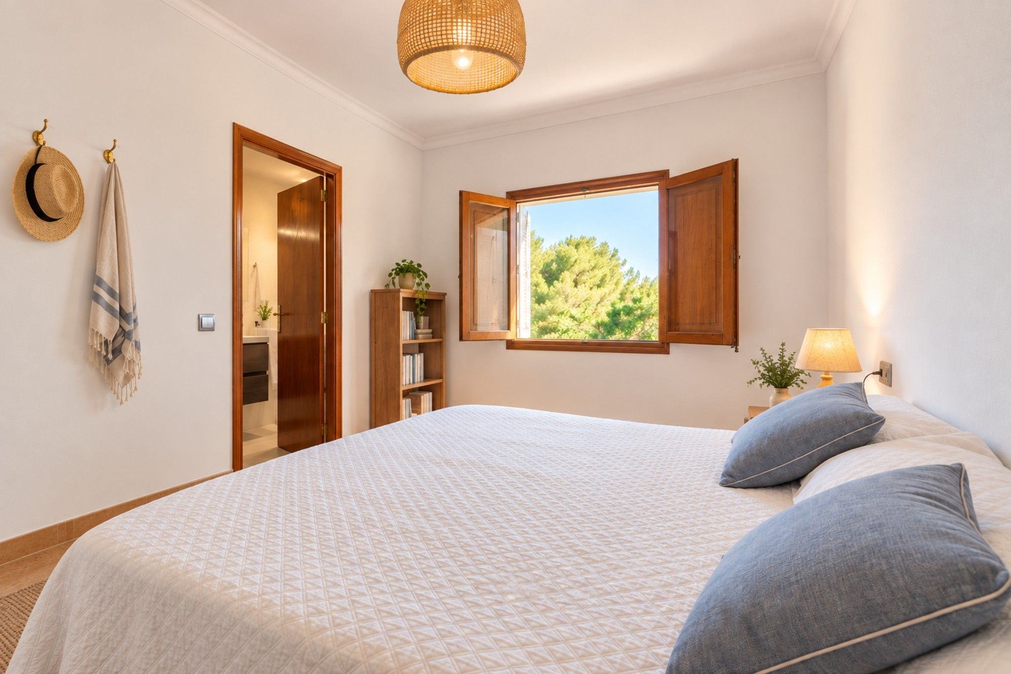 Ein Schlafzimmer mit einem großen Bett, einem Fenster mit geöffnetem Rollo, einem Kleiderschrank und einem Nachttisch mit Lampe.