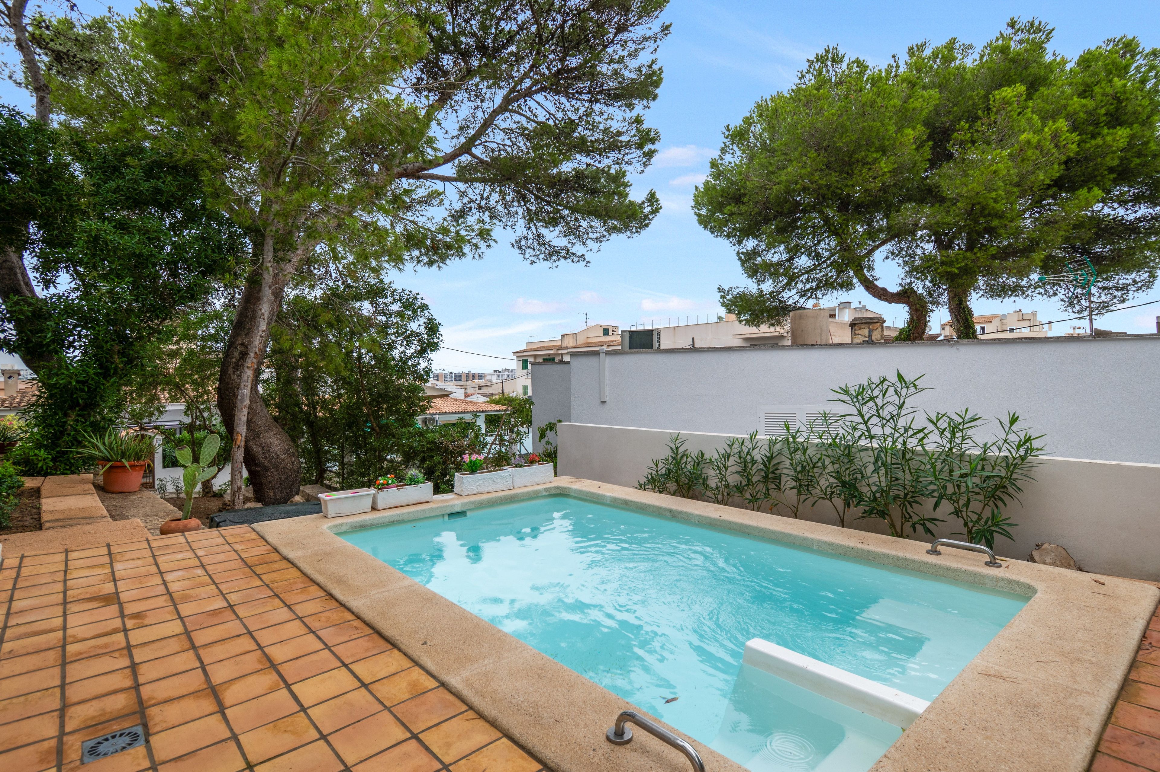 Une piscine dotée d’une terrasse carrelée, entourée de verdure et bordée d’un mur blanc.