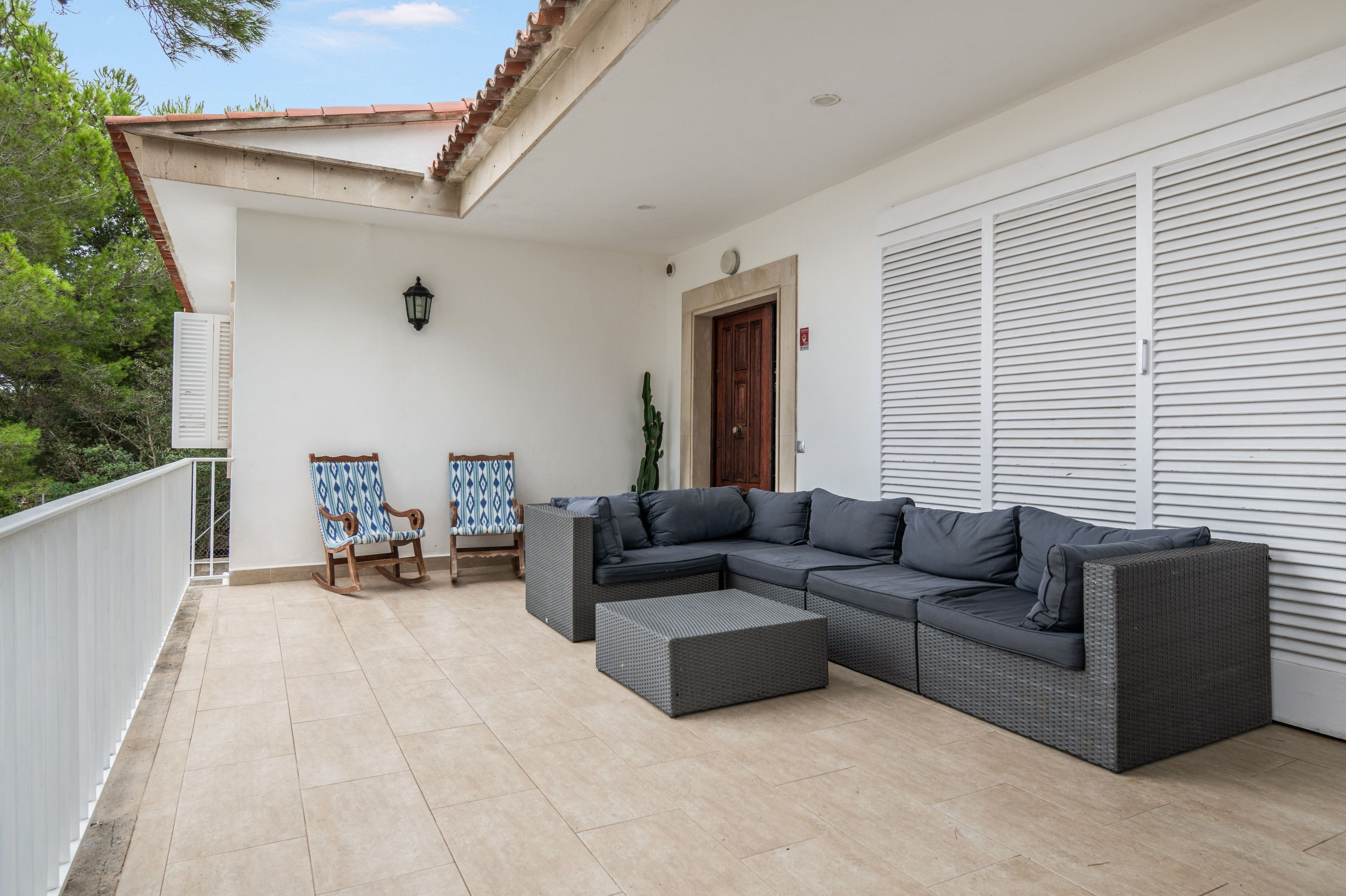 A covered outdoor seating area with a sectional sofa and two rocking chairs.