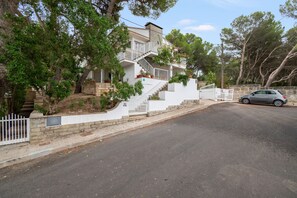 A residential property with a multi-level staircase leading to a balcony, a car parked on the street, and a white fence.