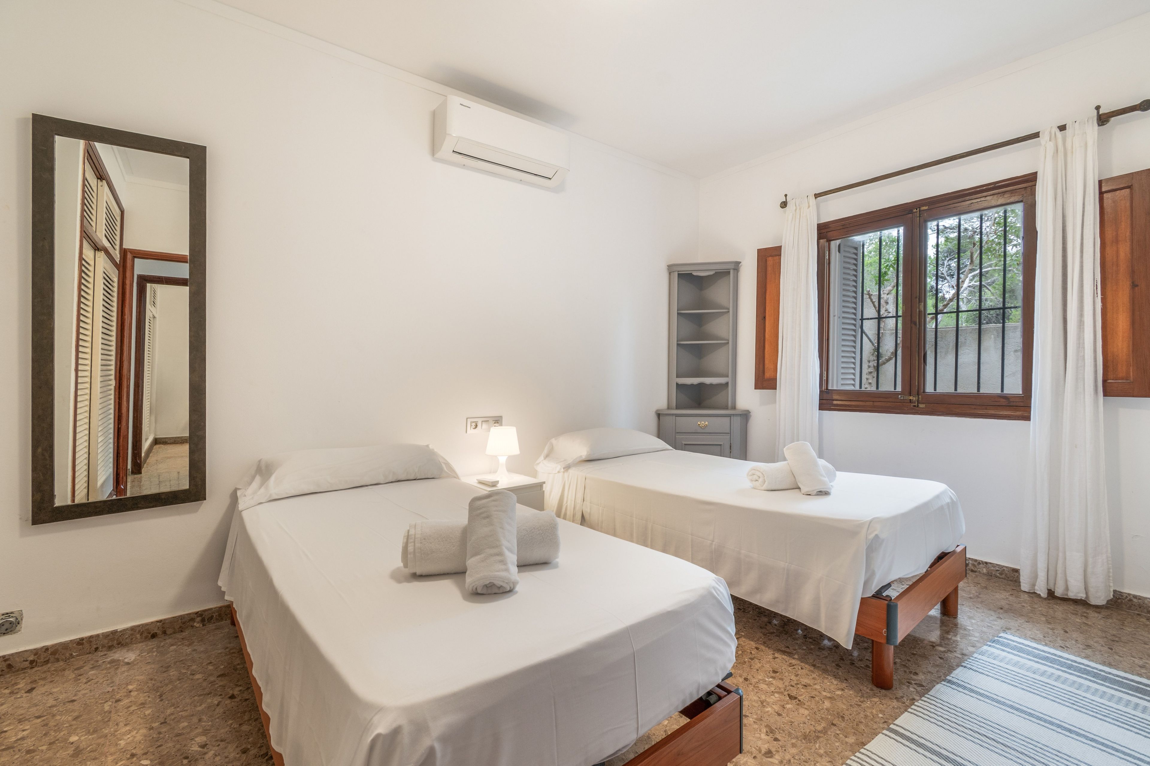 Une chambre d’hôtel avec deux lits, un miroir, une table de chevet avec une lampe, une armoire et une fenêtre avec des rideaux.