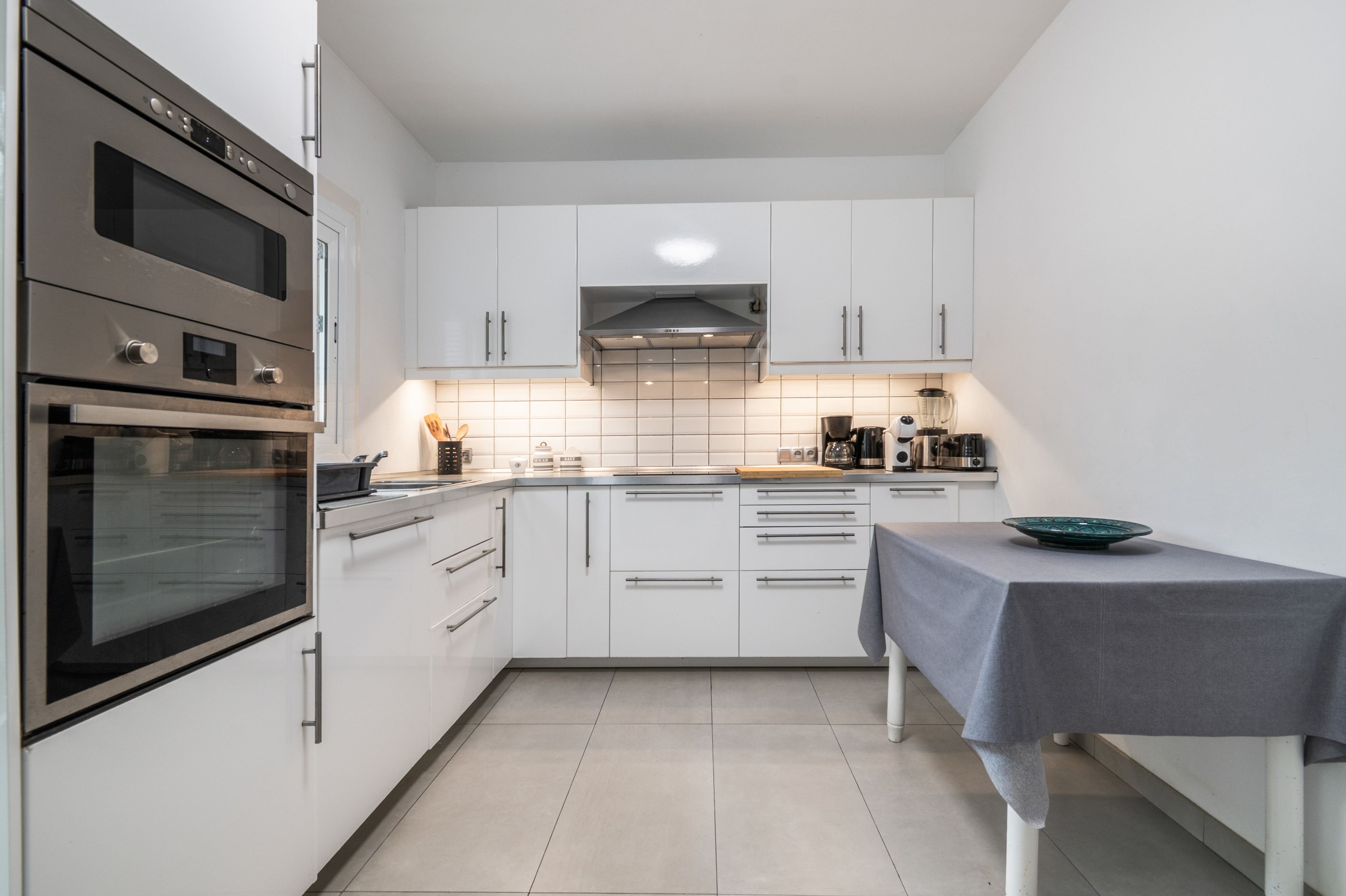 A modern kitchen with white cabinets, stainless steel appliances, and a tiled backsplash.