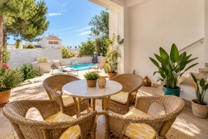 Eine Terrasse im Freien mit Korbmöbeln, einem Pool und Topfpflanzen.
