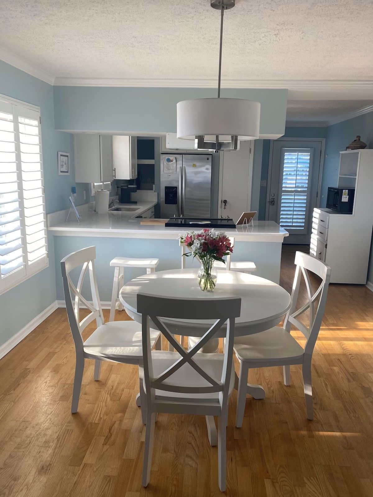 A modern kitchen with white cabinetry, a central island with seating, and a stainless steel refrigerator.