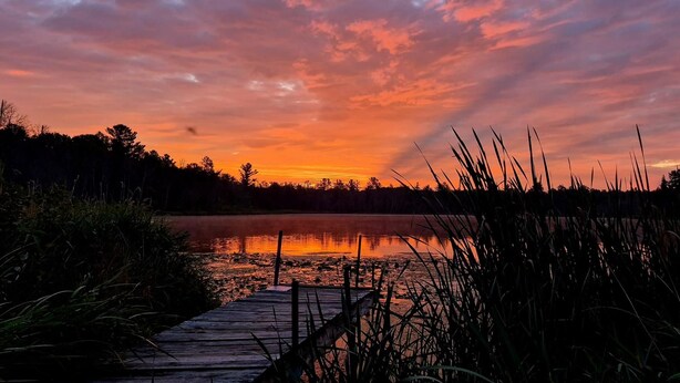 Puinen laituri, joka johtaa tyynelle järvelle, jonka yllä auringonlasku värjää taivaan.