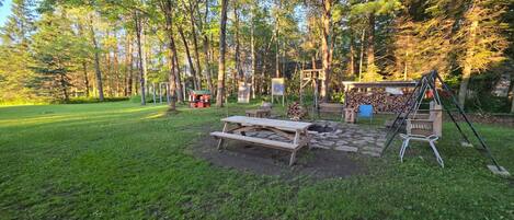 A picnic area with a table and benches, surrounded by trees and a small play structure.