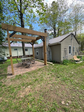 A backyard with a pergola, a patio table, and chairs. There is a small shed and a house in the background. - Peaceful Cabin Retreat on Lake Ann. 4-bedrooms perfect for relaxing getaway. (Stephenson)