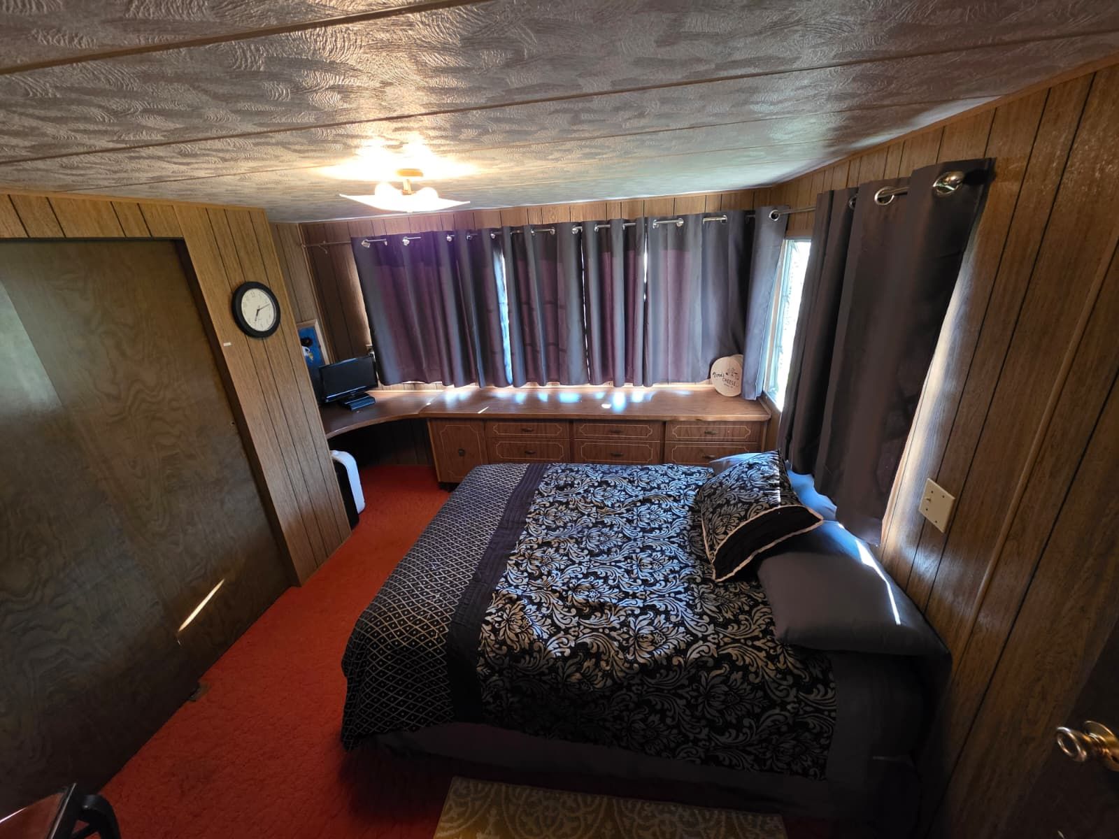 Une chambre à coucher de taille modeste, comprenant un lit, un bureau et une fenêtre avec des rideaux.