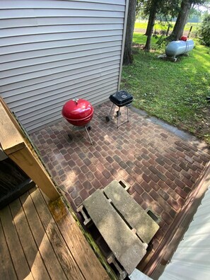 A patio with a brick floor, a red barbecue grill, and a portable grill cart.