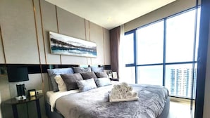 Une chambre d’hôtel moderne avec un grand lit, une table de chevet, un tableau accroché au mur et une grande fenêtre donnant sur la ville.