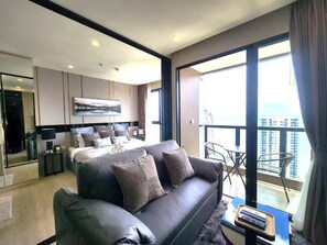 A modern hotel room with a large bed, a sofa, a balcony with a view, and a dining area. - The Panora Condominium Pattaya (Pattaya City)