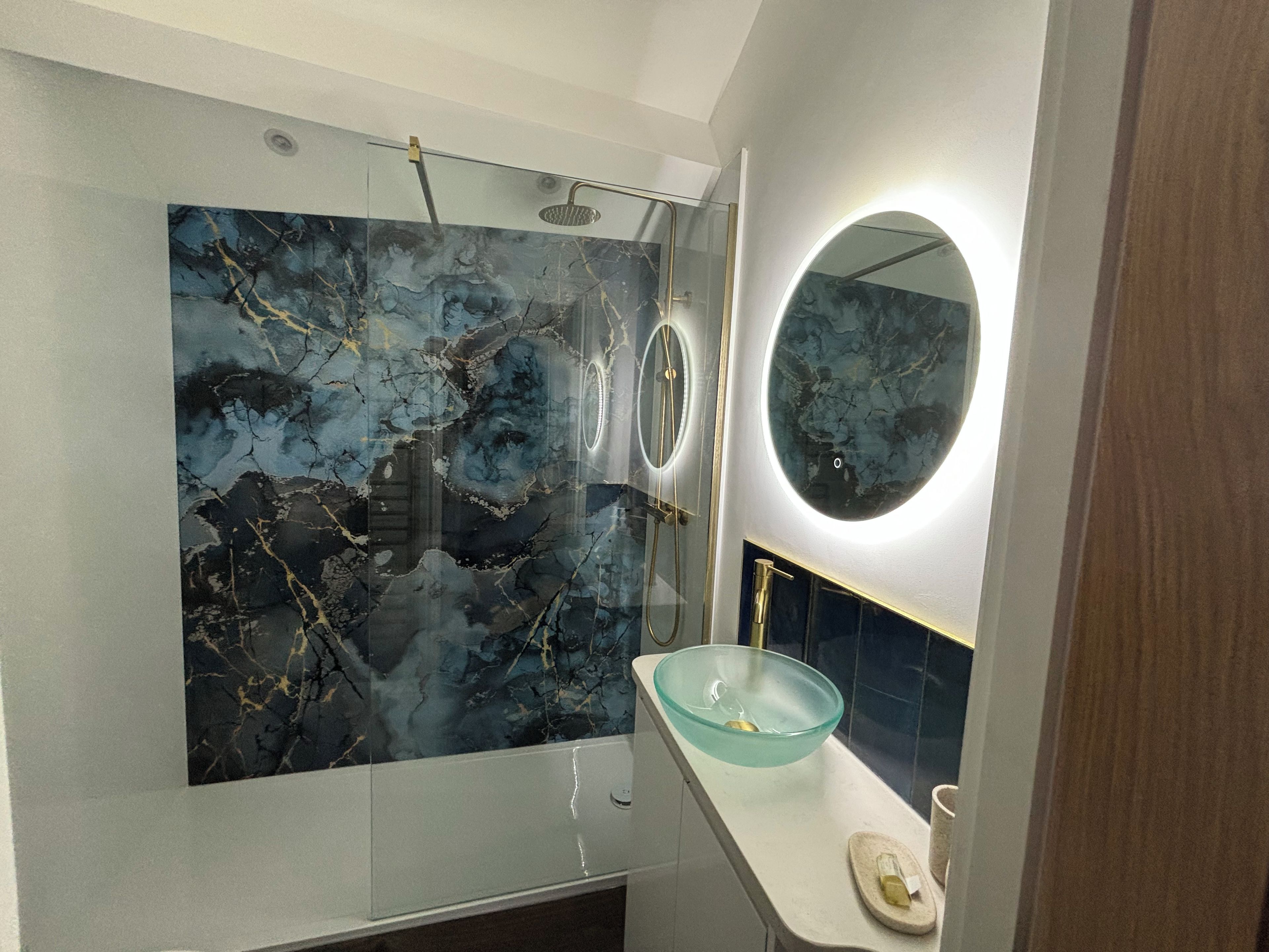 A bathroom with a glass shower enclosure, a marble backsplash, a round mirror, and a modern sink.
