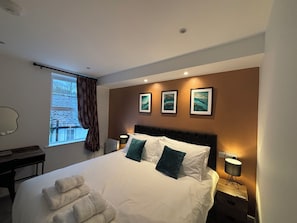 A hotel room with a large bed, a desk, and a window with curtains. - Braithwaite House Rooms (Keswick)