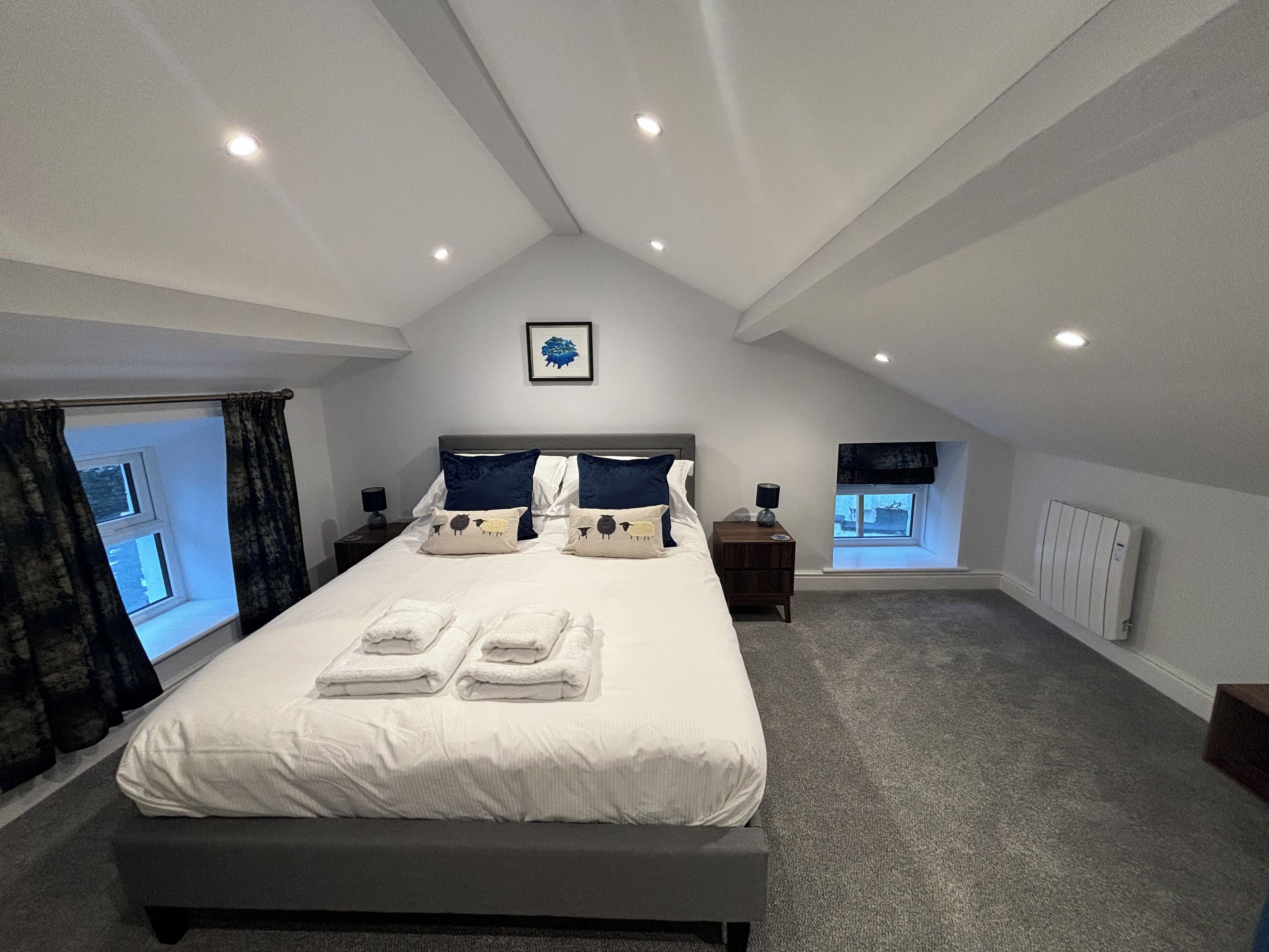 A bedroom with a large bed, two bedside tables, a window with curtains, and a radiator.