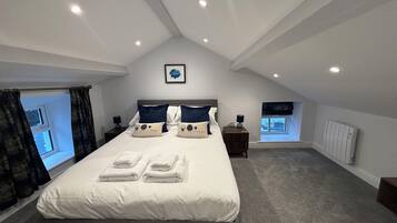 A bedroom with a large bed, two bedside tables, a window with curtains, and a radiator.