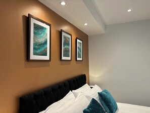 Una habitación de hotel moderna con una cama grande, tres obras de arte enmarcadas en la pared e iluminación empotrada en el techo.