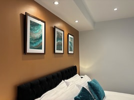 Una habitación de hotel moderna con una cama grande, tres obras de arte enmarcadas en la pared e iluminación empotrada en el techo.