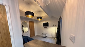 A compact living space with a wooden table, a television, a floor lamp, and a mirror. - Braithwaite House Rooms (Keswick)