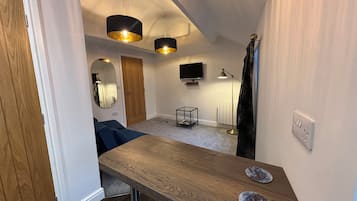 Un espace de vie compact comprenant une table en bois, un téléviseur, une lampe sur pied et un miroir.