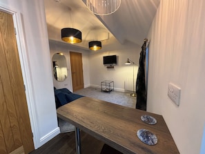 A compact living space with a wooden table, a television, a floor lamp, and a mirror. - Braithwaite House Rooms (Keswick)