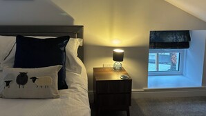 A bedroom with a bed, a bedside table with a lamp, a window with a view, and a framed picture on the wall. - Braithwaite House Rooms (Keswick)