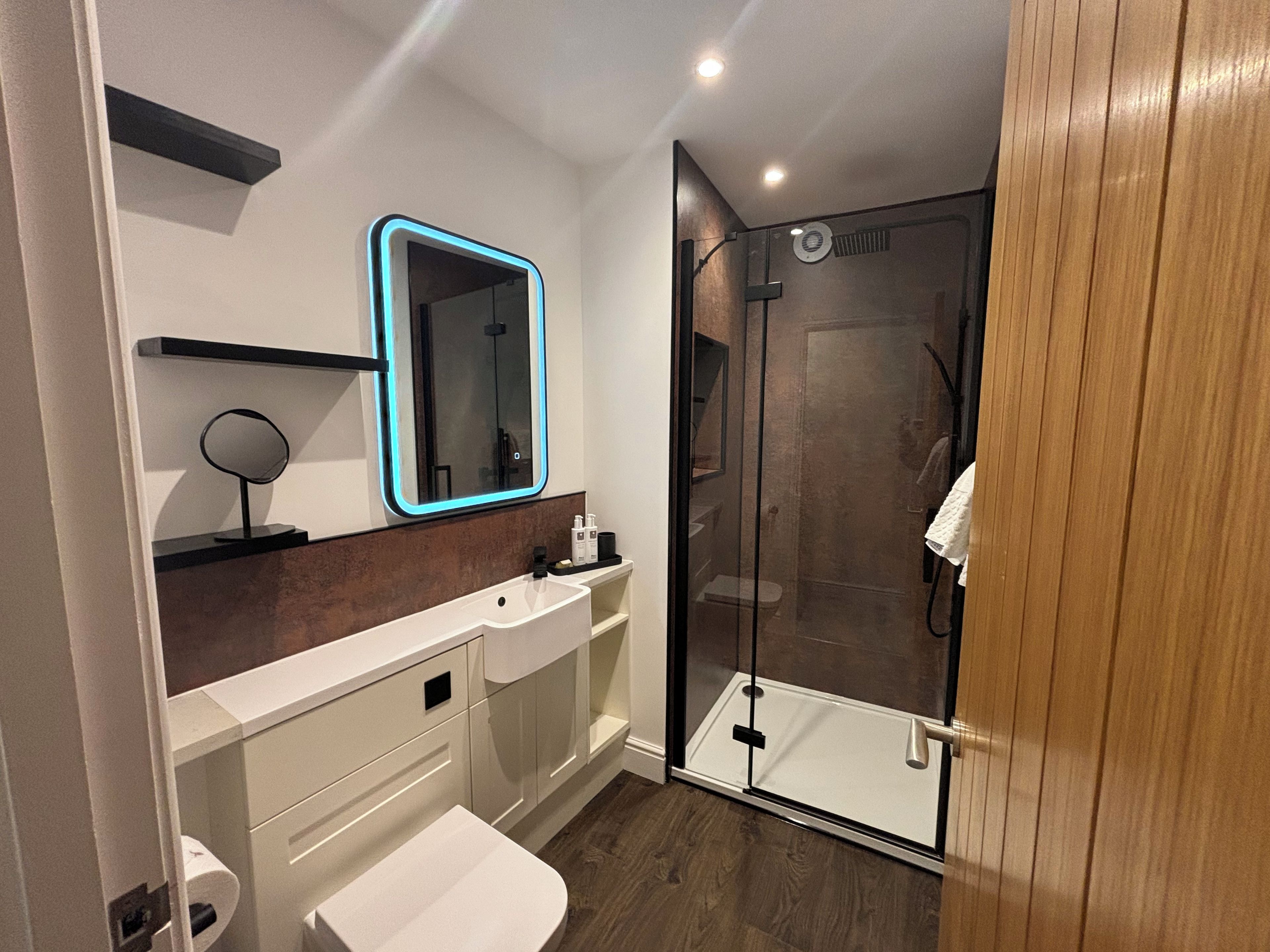 A modern bathroom with a glass shower enclosure, a white sink, and a mirror with a blue frame.