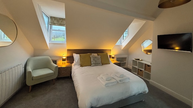 A bedroom with a bed, a chair, a TV, and a window. - Braithwaite House Rooms (Keswick)
