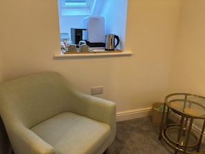 A room with a light green armchair, a coffee maker, and a small table with a glass top.