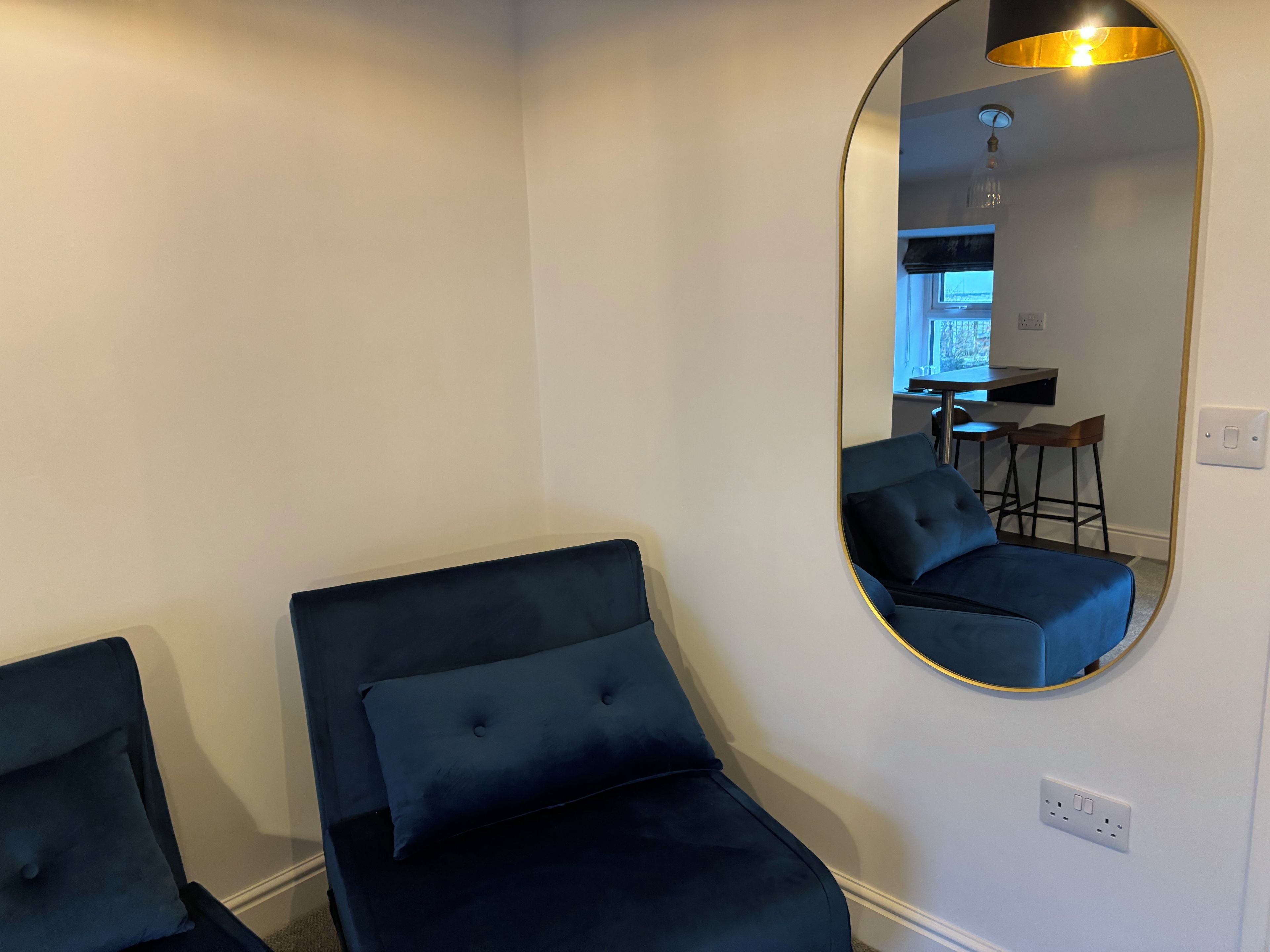 Quarto com um espelho grande refletindo uma área de cozinha compacta, uma cama com cabeceira e uma tomada na parede.