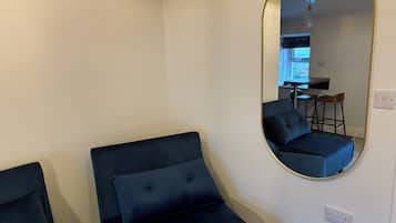 Quarto com um espelho grande refletindo uma área de cozinha compacta, uma cama com cabeceira e uma tomada na parede.