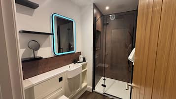 A modern bathroom with a glass shower enclosure, a white sink, and a mirror with a neon frame.