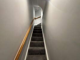 Una escalera con peldaños alfombrados y barandilla de madera, que asciende en un pasillo estrecho.
