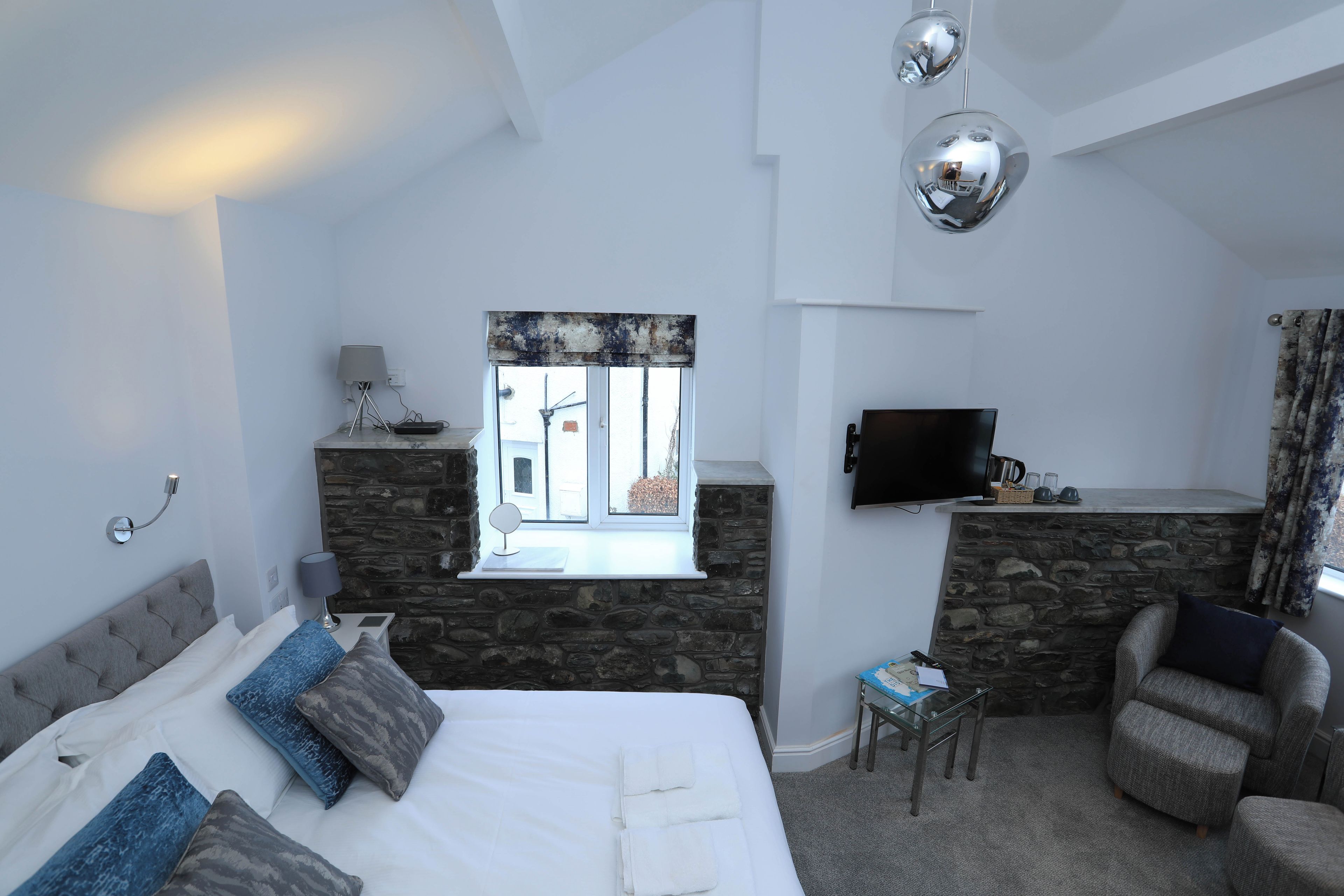 A modern bedroom with a bed, a stone wall, a window, a television, and a seating area.