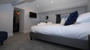 A modern bedroom with a large bed, a flat-screen TV, and a ceiling-mounted light fixture. - Braithwaite House Rooms (Keswick)